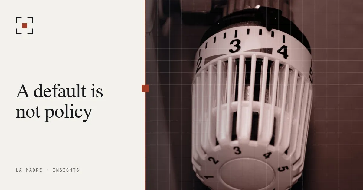 A radiator thermostat dial set near the middle of its range, in La Madre duotone, beside the words A default is not policy