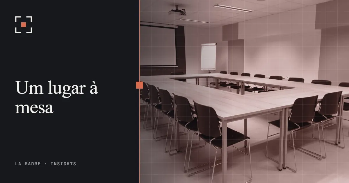 Uma sala de reunião vazia com mesas dispostas em U e cadeiras ao redor, em duotone La Madre, ao lado das palavras Um lugar à mesa