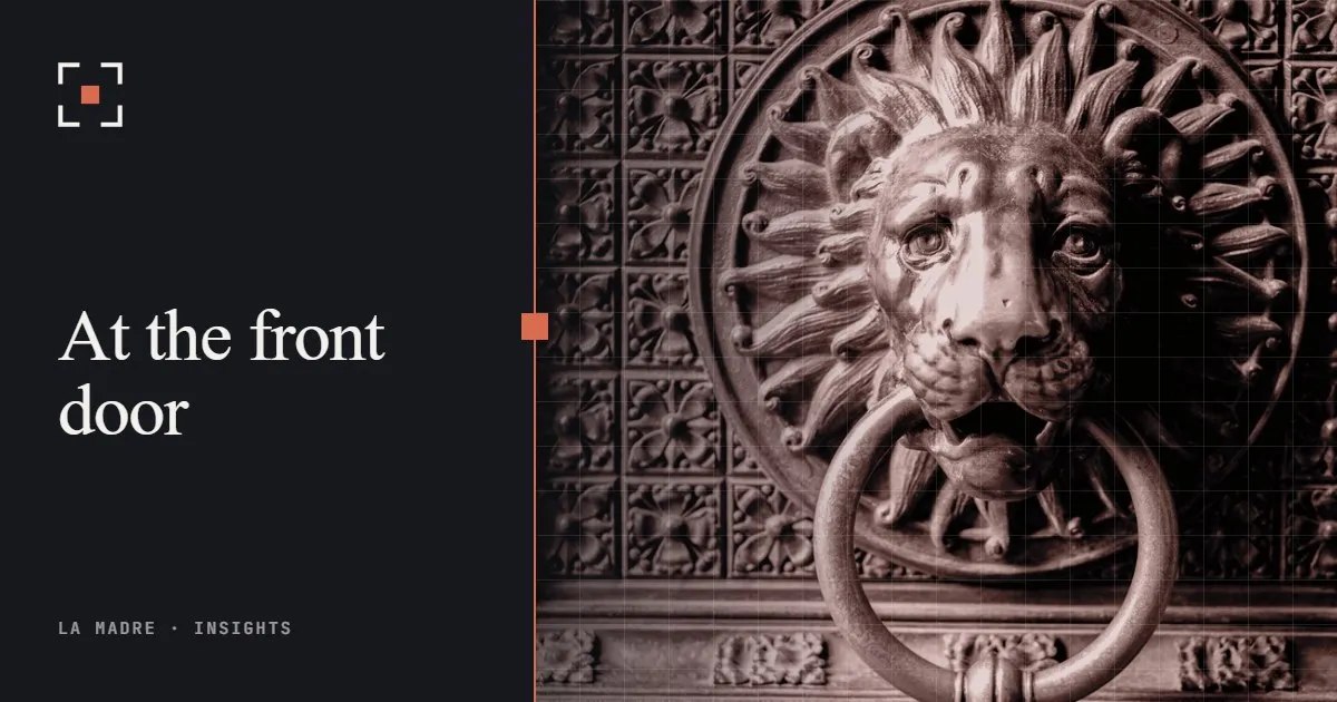 A brass lion door knocker on an ornate door, in La Madre duotone, beside the words At the front door