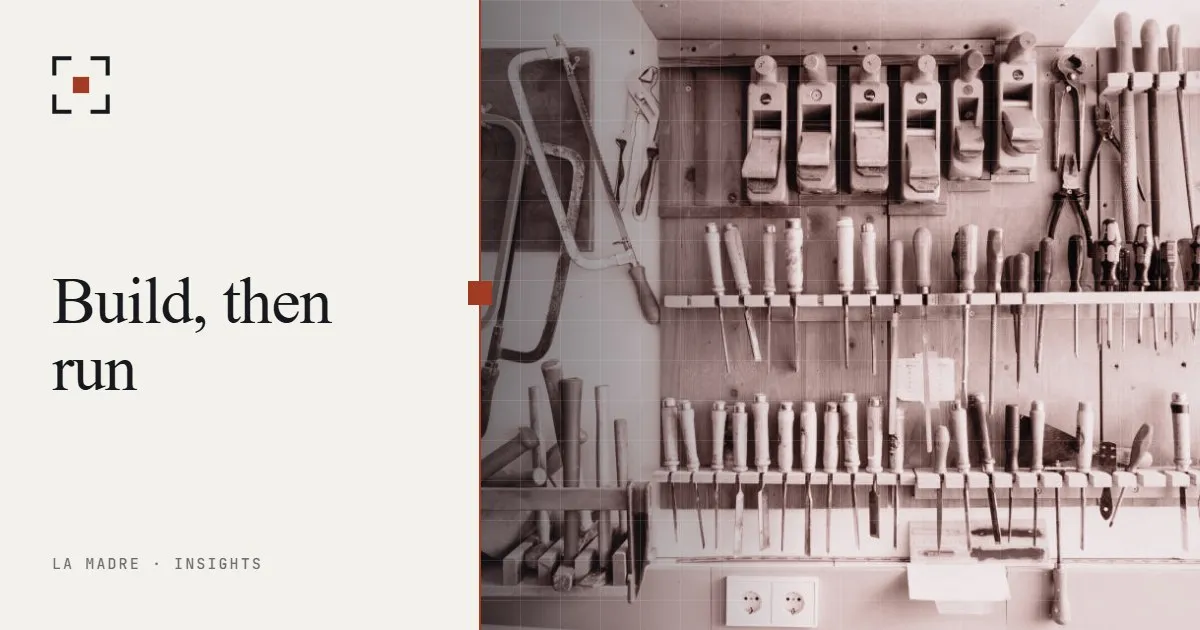 Organized wall of workshop tools, in La Madre duotone, beside the words Build, then run