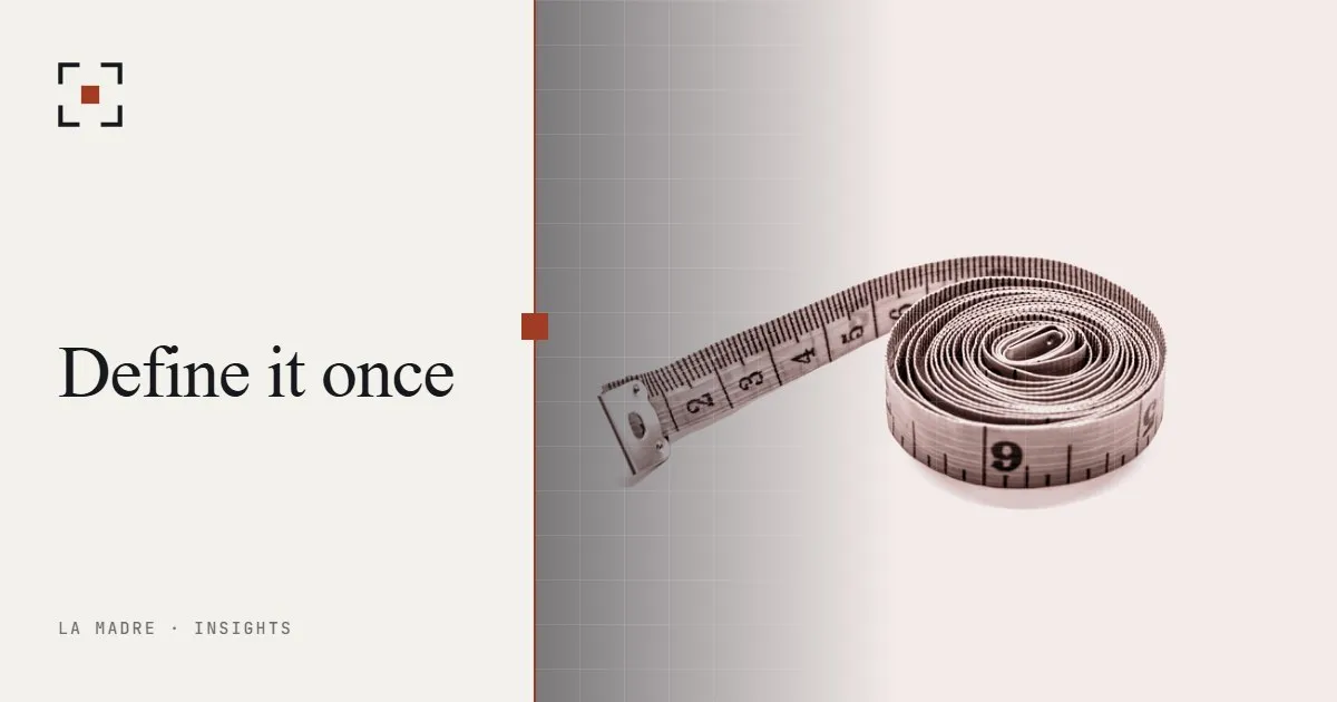 A coiled tape measure on a white surface, in La Madre duotone, beside the words Define it once